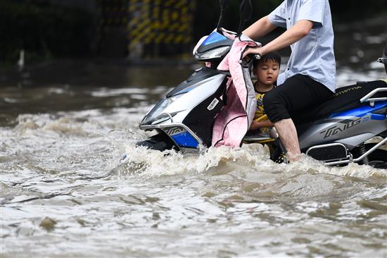 7月4日，河南省郑州市，一场突如其来的暴雨，让路成“海”。由于积水较深，有人骑电动车通过，有人抱着孩子走过去，还有被朋友背过去…… IC 图